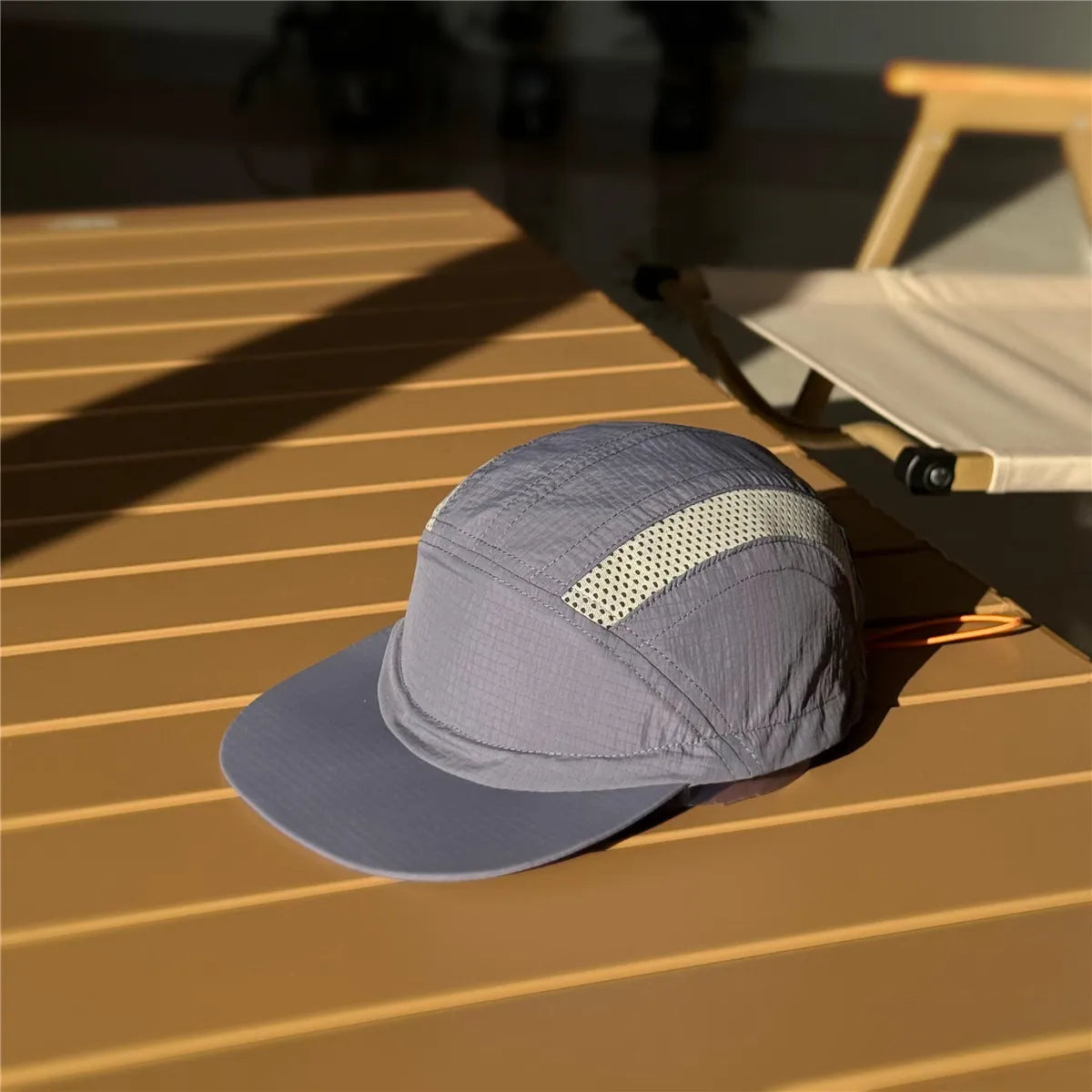 Nylon running cap in slate grey on a sunlit table, with grey mesh inserts and an orange rear drawcord.