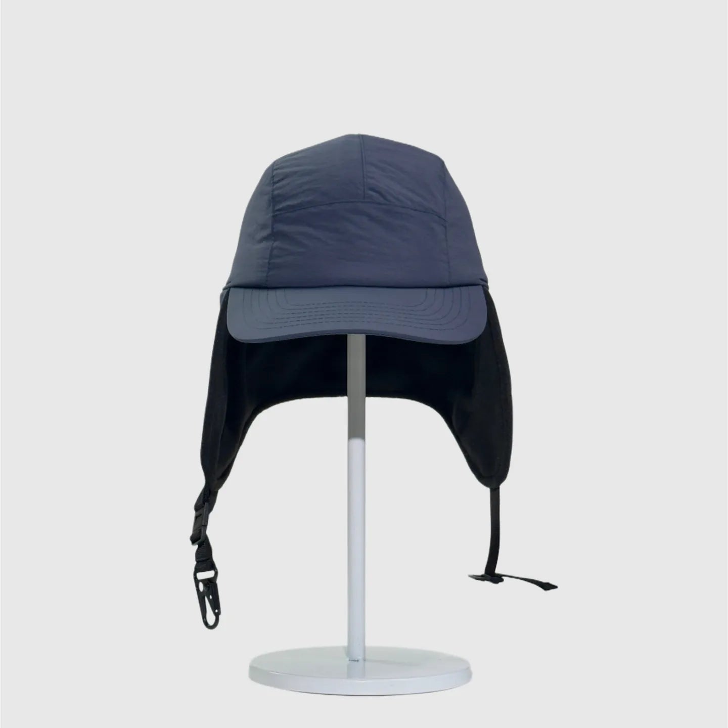 Navy nylon winter ear flap cap front view with extended side covers, stitched brim and buckle straps.
