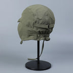 Rear side view of an olive green ear flap cap with a back strap and elasticated lower edge