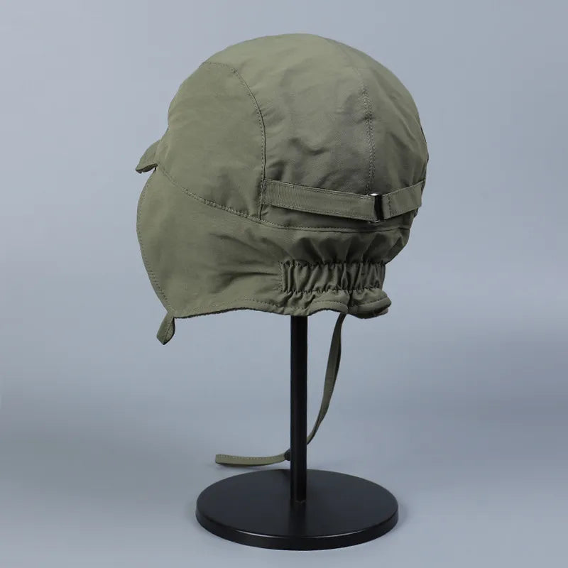 Rear side view of an olive green ear flap cap with a back strap and elasticated lower edge