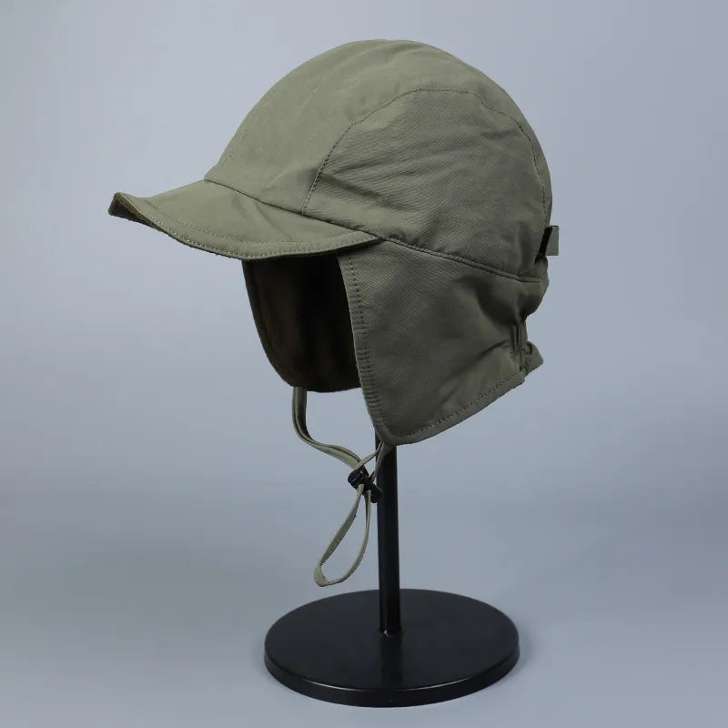 Olive green winter ear flap cap shown from the side with a curved brim and adjustable chin tie.