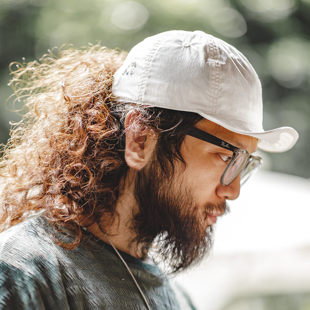 Beige nylon outdoor cap worn by a man in natural sunlight, showing the lightweight panelled design