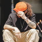 Man styling an orange nylon baseball cap with a black T-shirt and beige cargo trousers