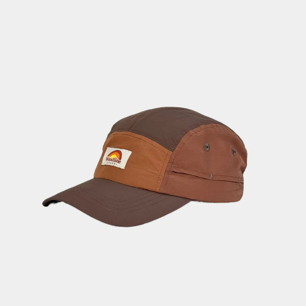 Panelled camper cap in dark brown, burnt orange and chestnut, angled view with a woven badge and curved peak