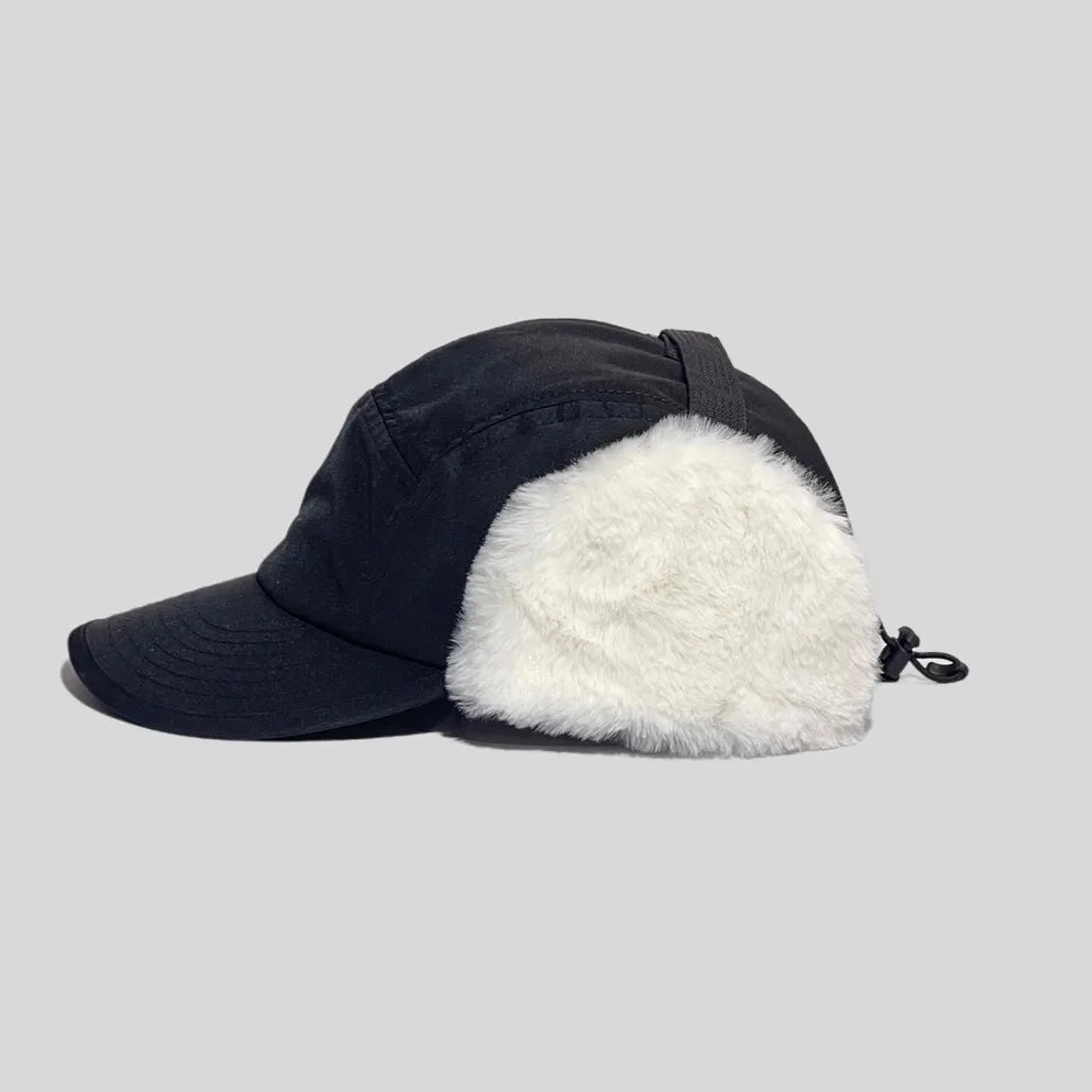 Polyester trapper cap in black, side profile with a curved peak, white faux-fur ear flap and rear cord lock
