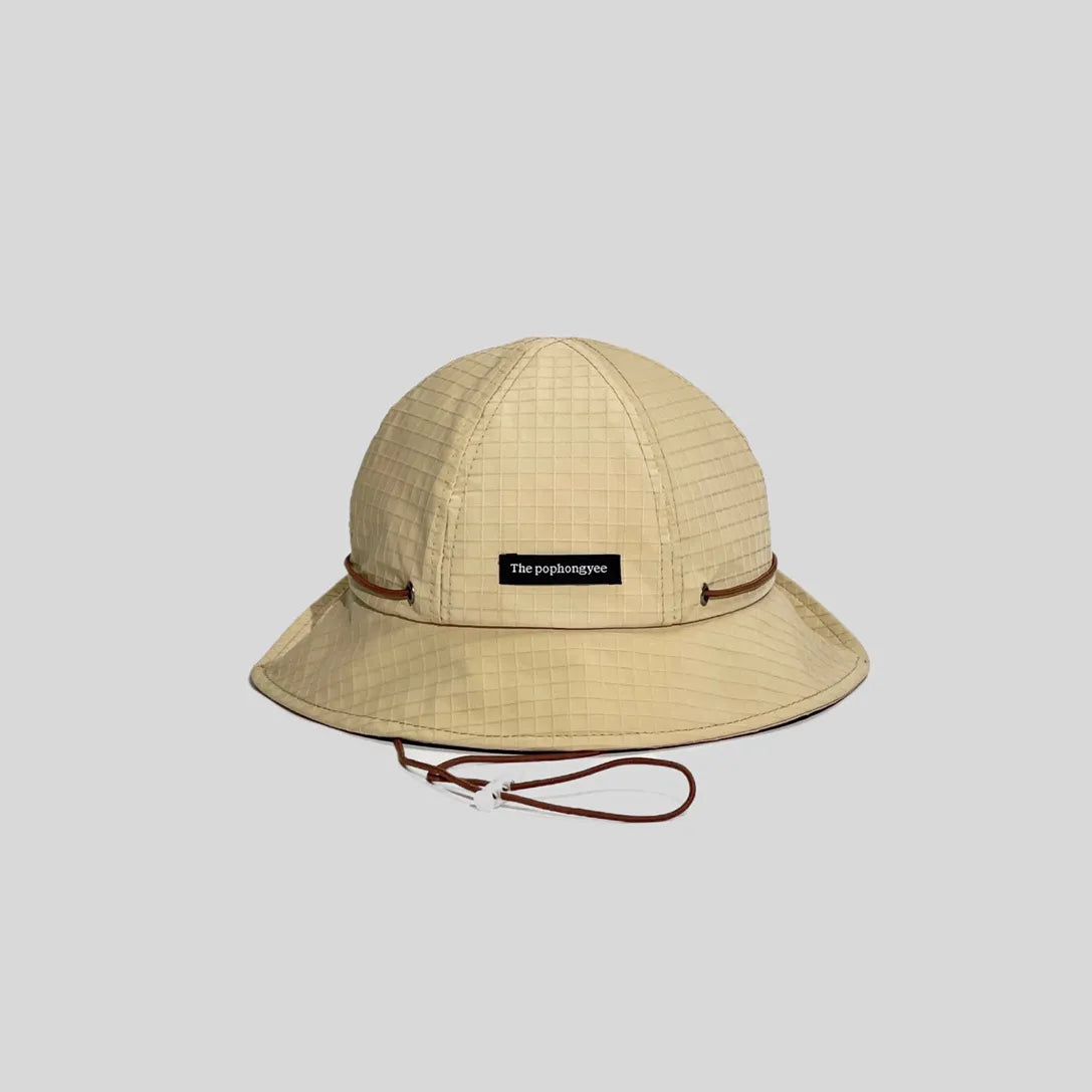 Quick-dry bucket hat in sand beige with a brown cord, front view showing the logo tab, grid weave and wide brim