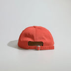 Back view of a red baseball cap with an open back, ventilation eyelets and an adjustable metal buckle strap.