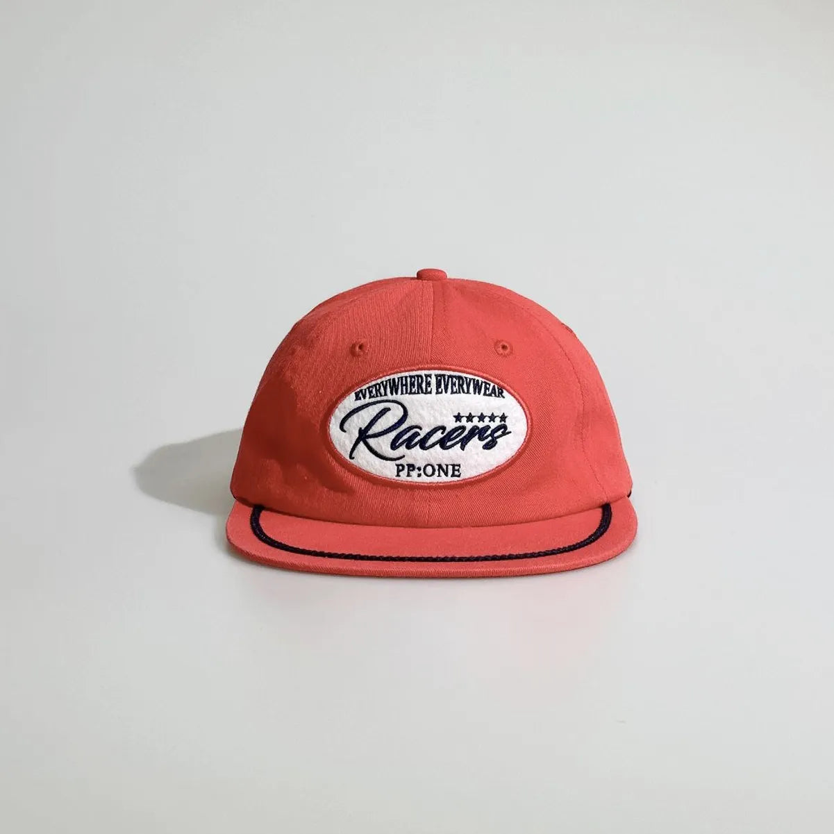 Front view of a red baseball cap featuring an oval racing patch, black rope detail and a stitched brim for everyday casual wear.