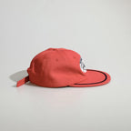 Side profile of a red baseball cap showing the panelled crown, oval racing patch, black rope trim and adjustable back strap.