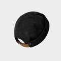 Rear view of a black cotton corduroy docker cap with ribbed texture, brown adjustable strap and metal snap details
