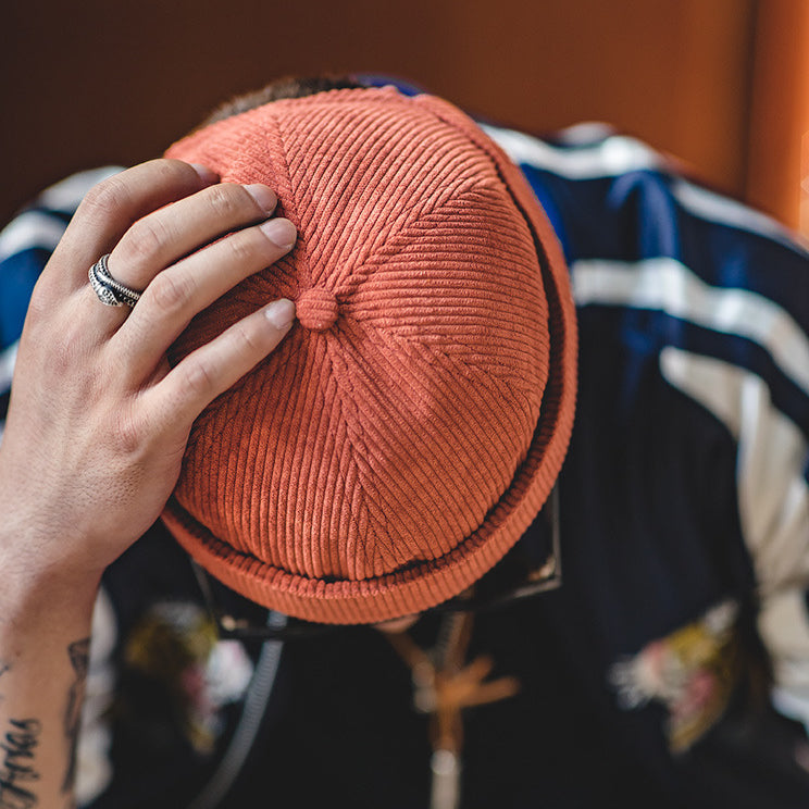 Top view of a rust cotton corduroy sailor cap with ribbed texture, panelled crown and covered top button