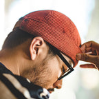 Side view of a man wearing a rust cotton corduroy brimless docker hat with a folded cuff