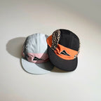 Close-up product view of black and orange and light blue and pink five-panel caps with animal print panels for casual streetwear styling.
