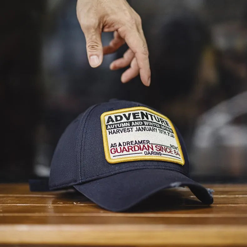 Man wearing a navy cotton baseball cap with an Adventure embroidered patch