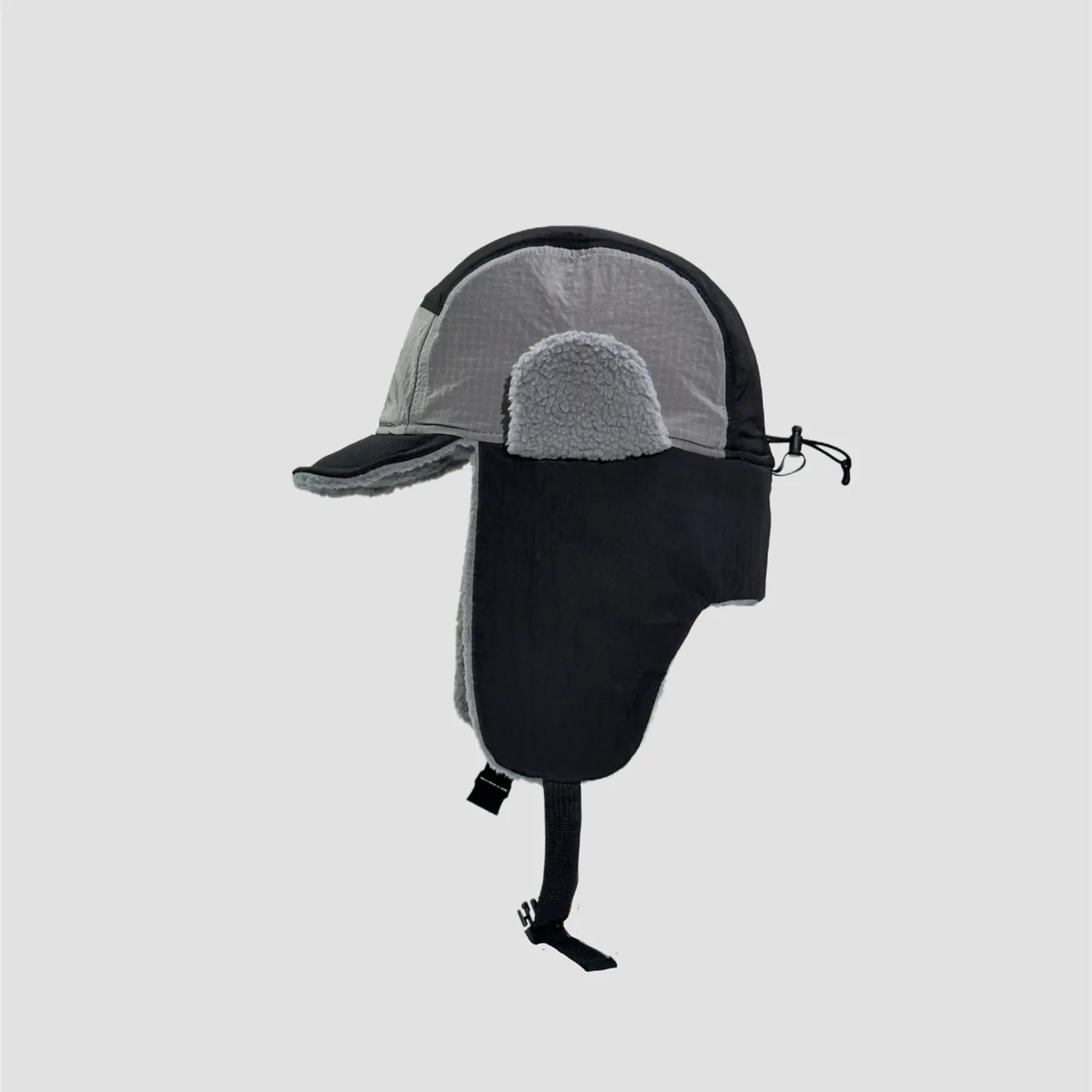 Black and grey waterproof trapper hat side view showing ripstop-style panels, plush ear detail and chin strap.