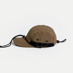 Waterproof outdoor cap in tan, side view with two metal eyelets, black webbing trim and an adjustable cord