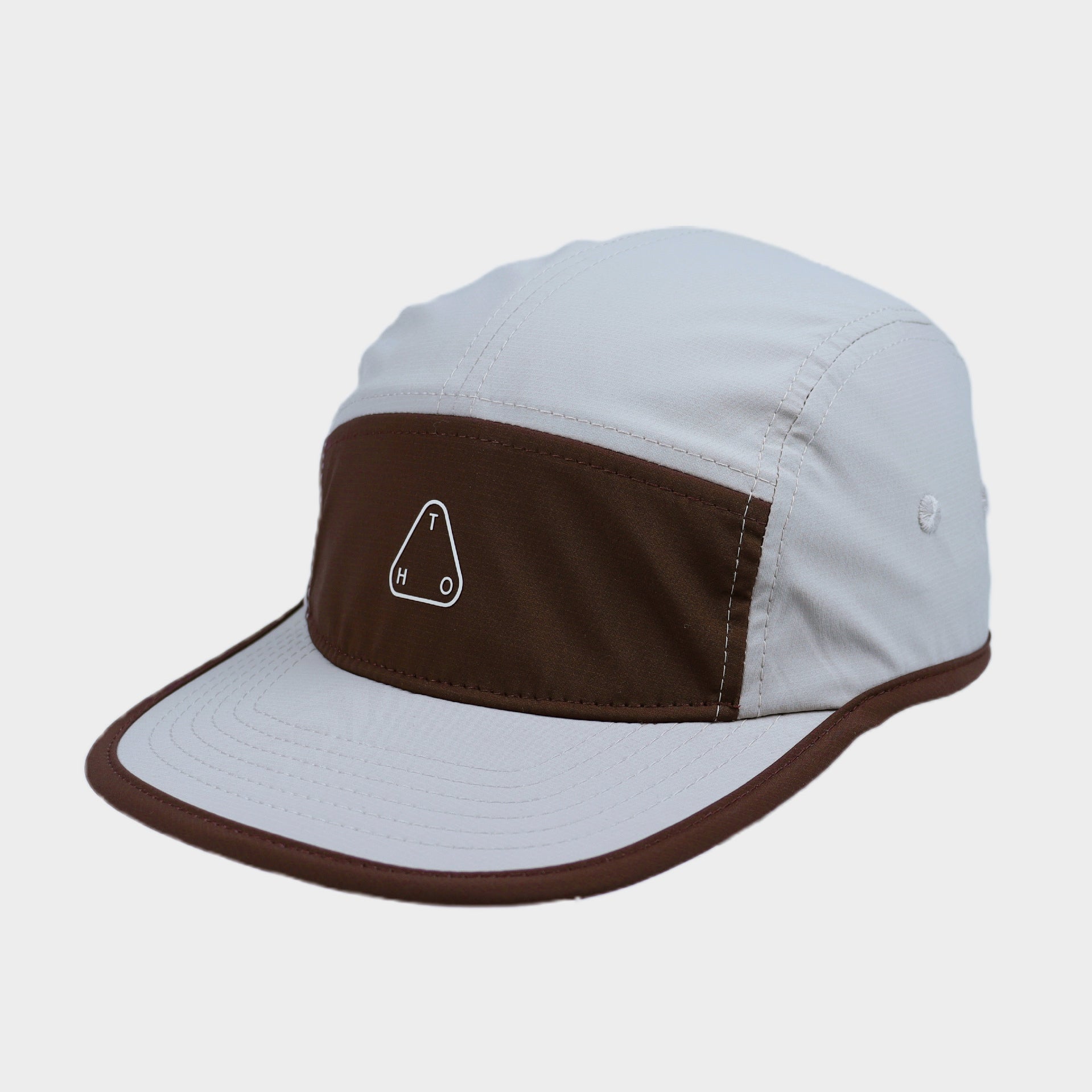 Close-up of a white and brown colour-block camp cap with a flat brim, contrast piping and minimalist triangular logo.