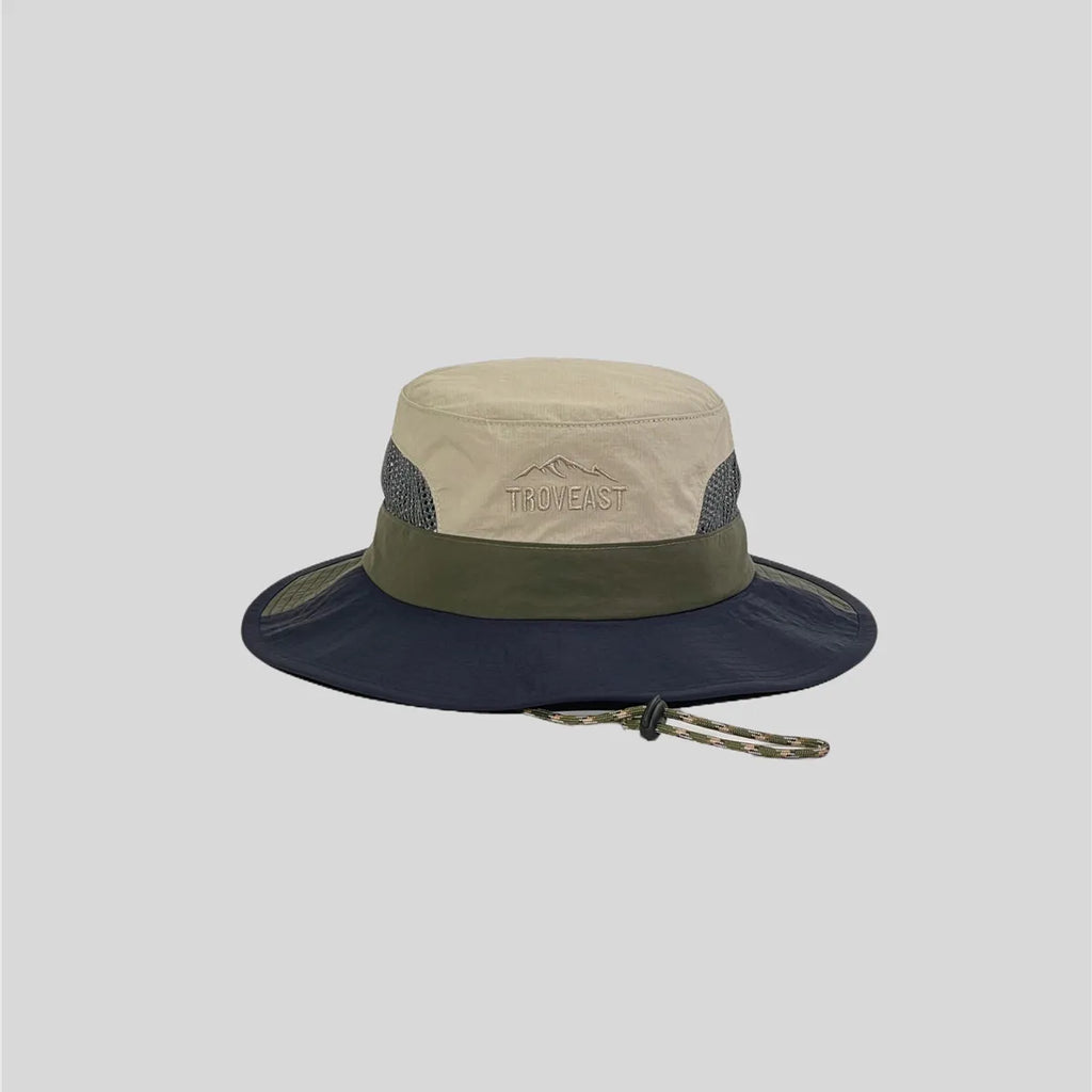 Beige wide-brim sun hat front view with olive band, navy brim, grey mesh panels and tonal mountain embroidery.