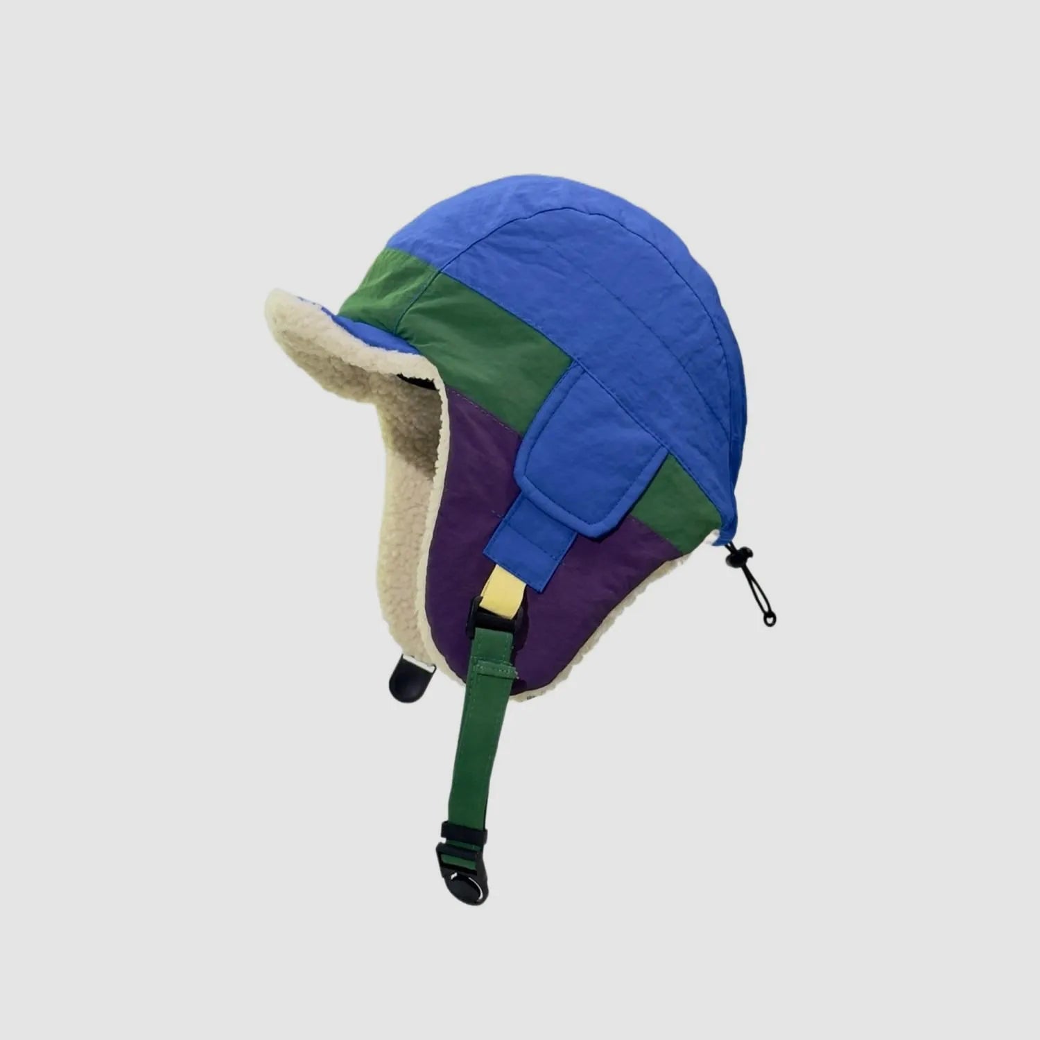 Blue and green winter ear flap cap side view with purple panels, cream fleece trim and adjustable chin strap.