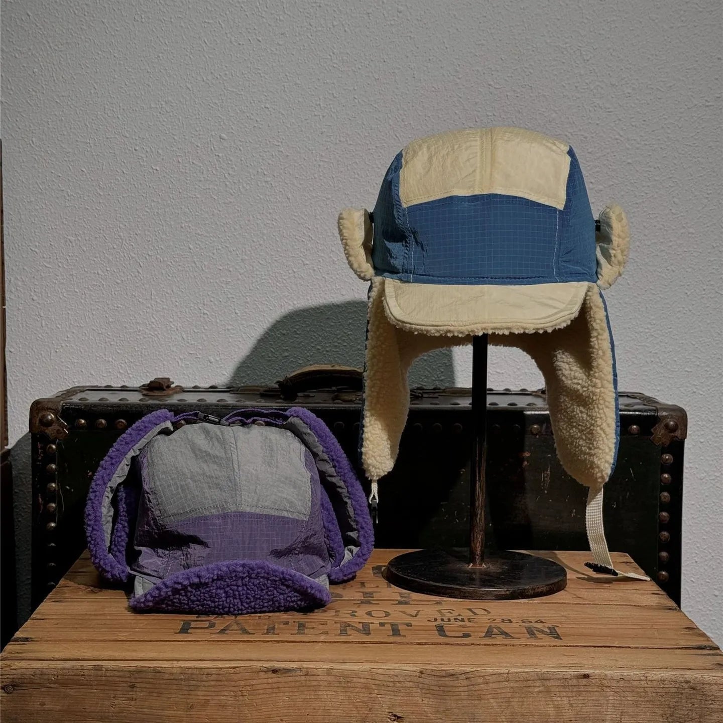 Blue and yellow plush-lined winter hat product scene with purple interior view displayed on a vintage wooden case.