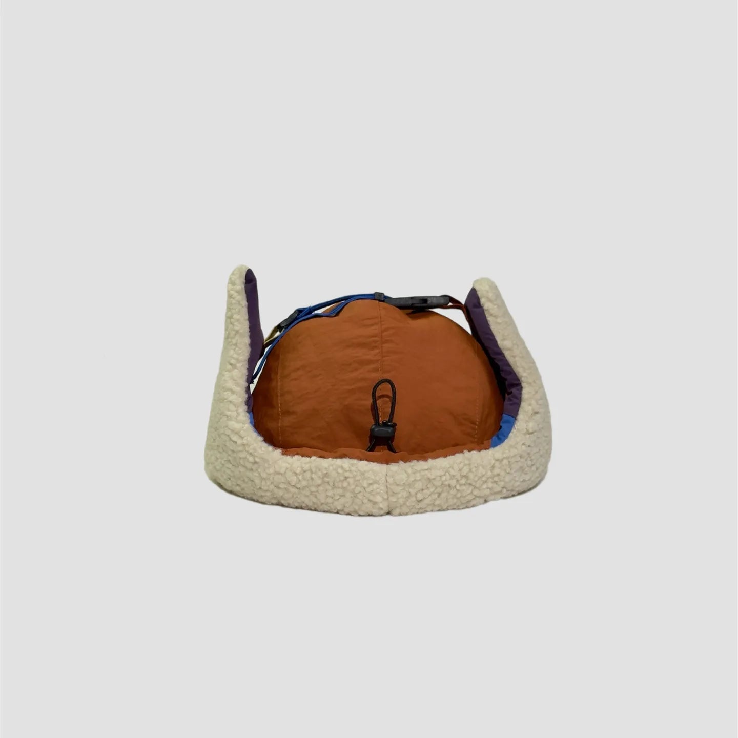Orange and blue winter trapper hat rear view with cream fleece ear flaps and adjustable chin strap.